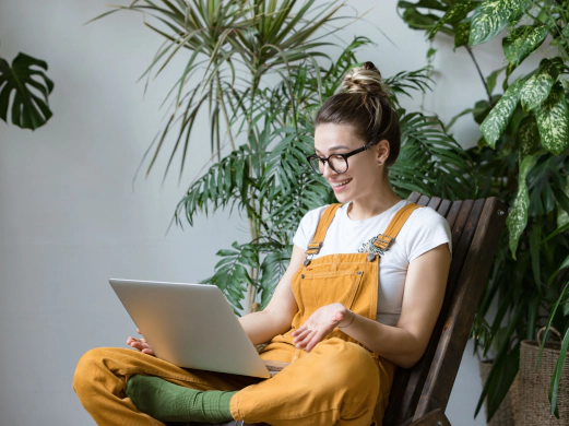 girl wearing yellow overalls working with her laptop among green plants